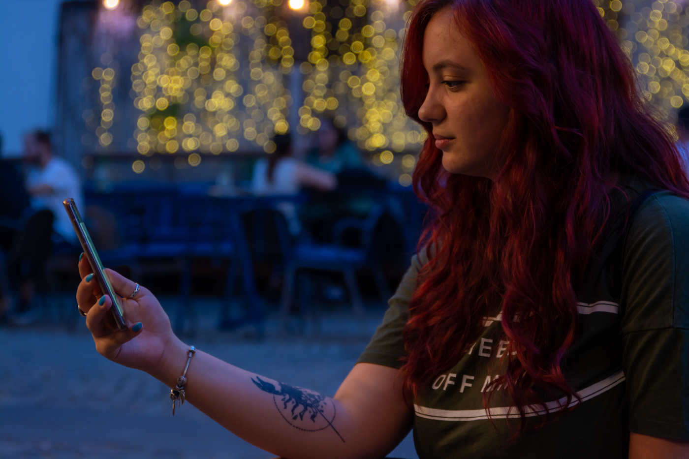 Femeie roscata cu parul lung si cu tatuaj tinand in mana un telefon